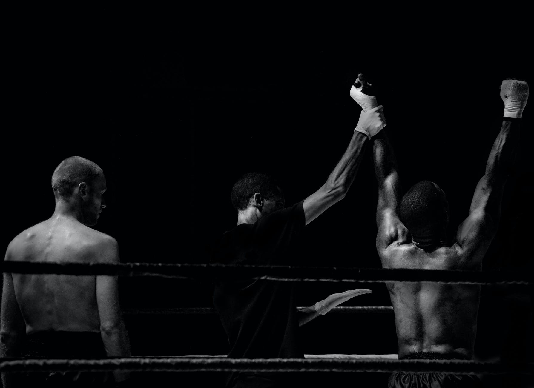 grayscale photography of man holding boxer s hand inside battle ring